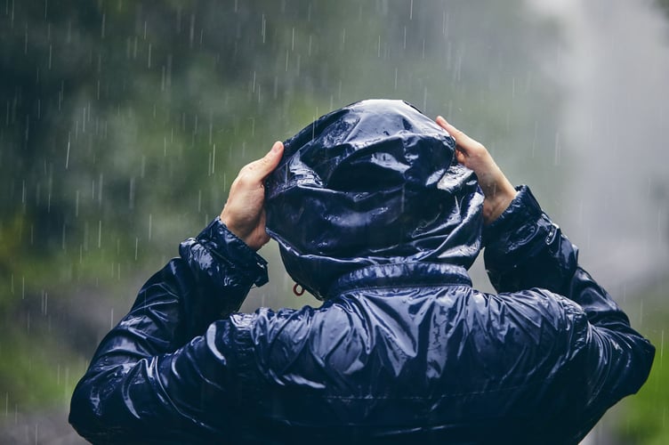 Trip in bad weather. Rear view of young man in drenched jacket in heavy rain.