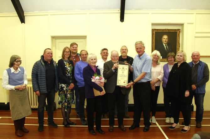 Tim Webb (centre) receives the 'Freedom of the Parish' from Old Cleeve Parish Council chairman Cllr Ian Duncan with his wife Jeanne beside him. Other councillors also attending were Geoffrey Williams, Di Binding, Rick Gaskin, Louise Baker, Matt Ensor, Margaret Smith, Steve Eggar, Chris Dutton, Phil Gannon, and Heather Beaver.